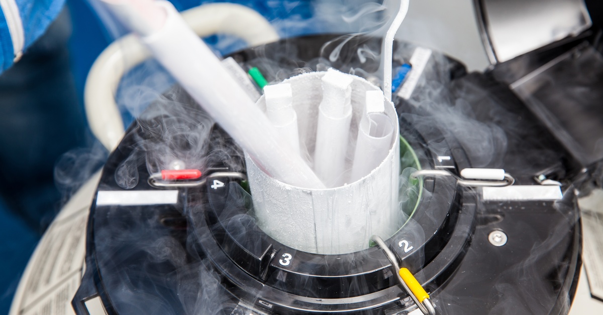 A liquid nitrogen cryogenic tank in a laboratory, emitting white vapor. The tank contains cylindrical tubes.