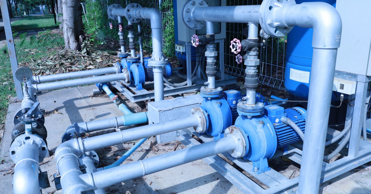 An outdoor industrial metal rotary valve with two pipes on a cement floor controlling fluid flow in a piping system.