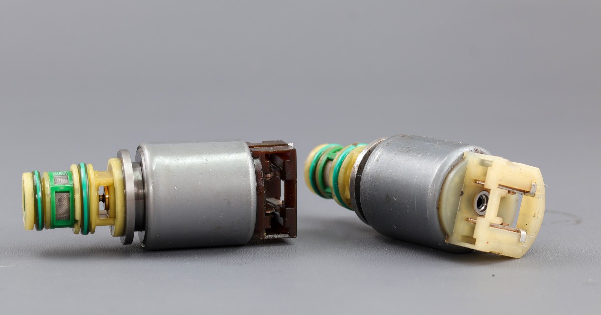 Two solenoid valves on a gray background, one upright and the other lying on its side, showcasing their components.