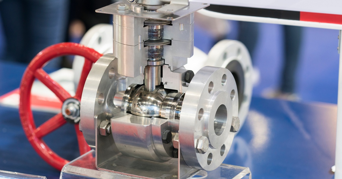 A metal industrial valve with visible internal components, including a spherical ball and flange, displayed on a clear base.