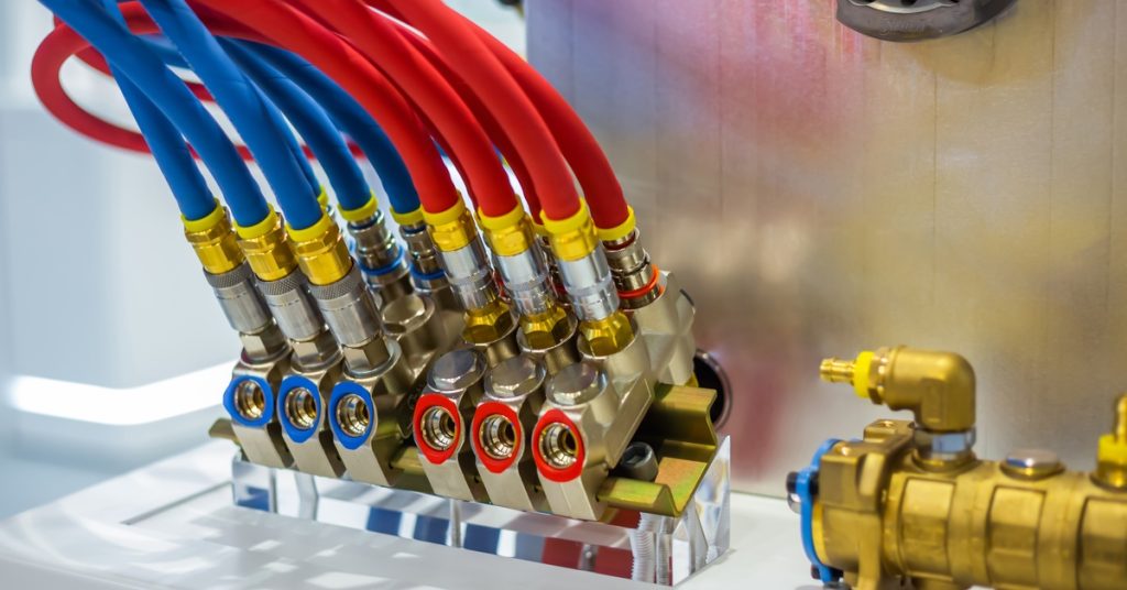 Red and blue hydraulic hoses and valves on a mold control system, part of an injection molding machine.