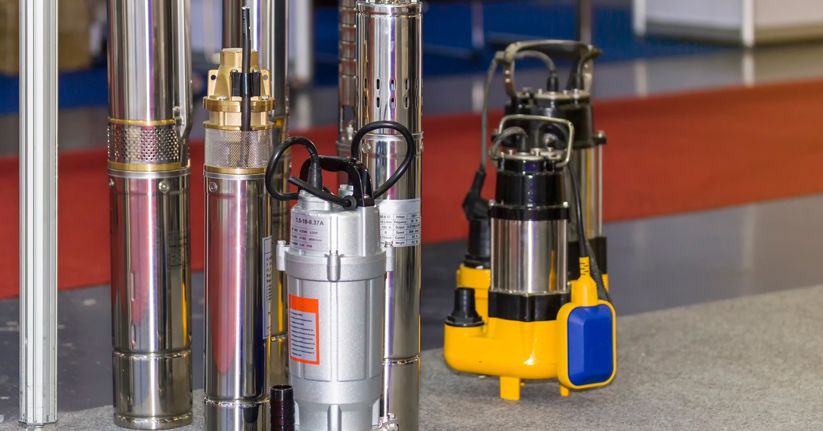 A collection of vertical industrial pumps and valves in different designs and colors, arranged on a gray ground surface.