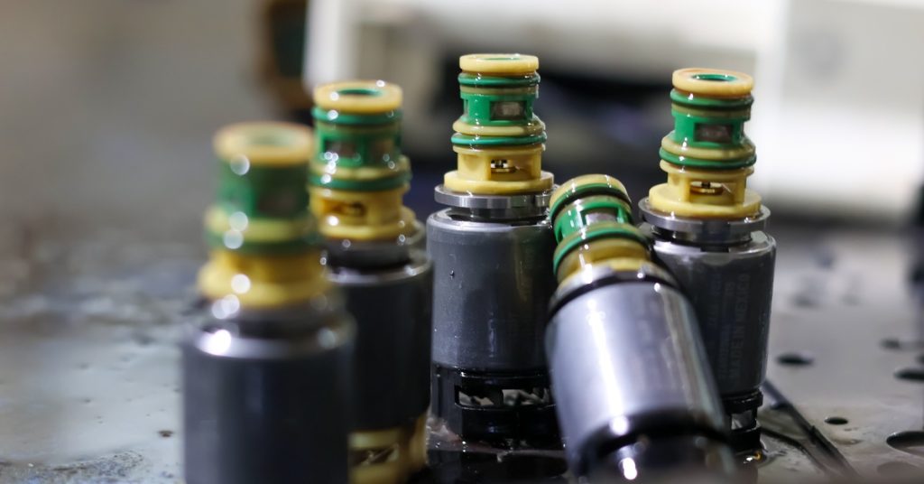 Four solenoid valves sit clustered together on a black surface, with one valve slightly tipping back.