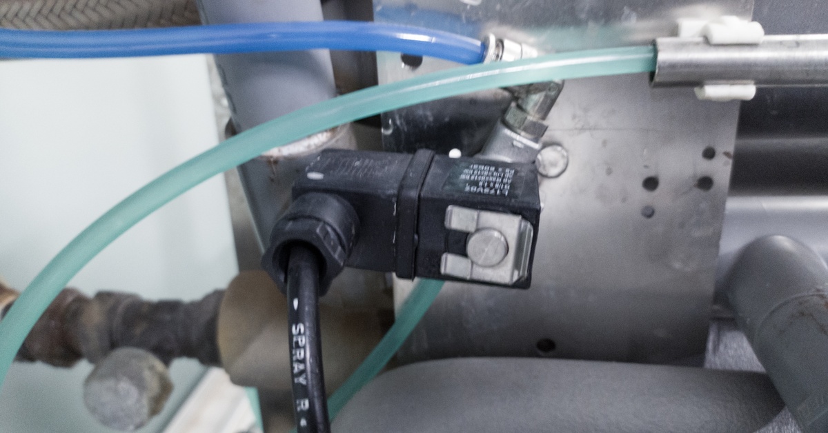 An installed solenoid valve connects to hoses and tubing inside a machine, with wires and fittings visible.