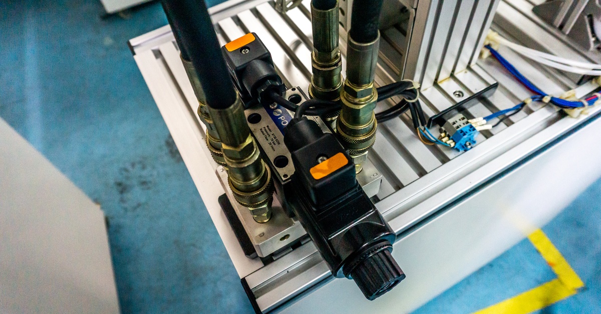 Multiple solenoid valves connect to vertical pipes on a metal base, with wiring and fittings arranged in an industrial setup.