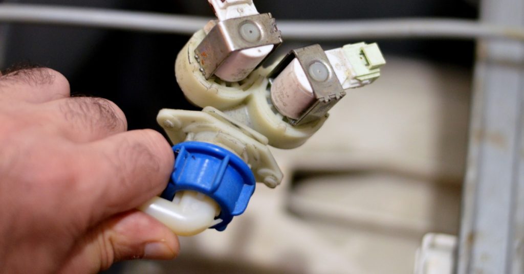 A blue and white inlet water valve rests on a surface beside tubing, wires, and small appliance parts.