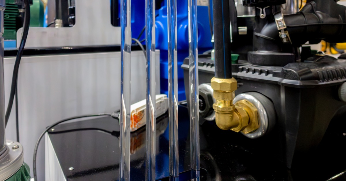 Clear vertical tubes and brass fittings attached to black machinery with blue equipment in the background.