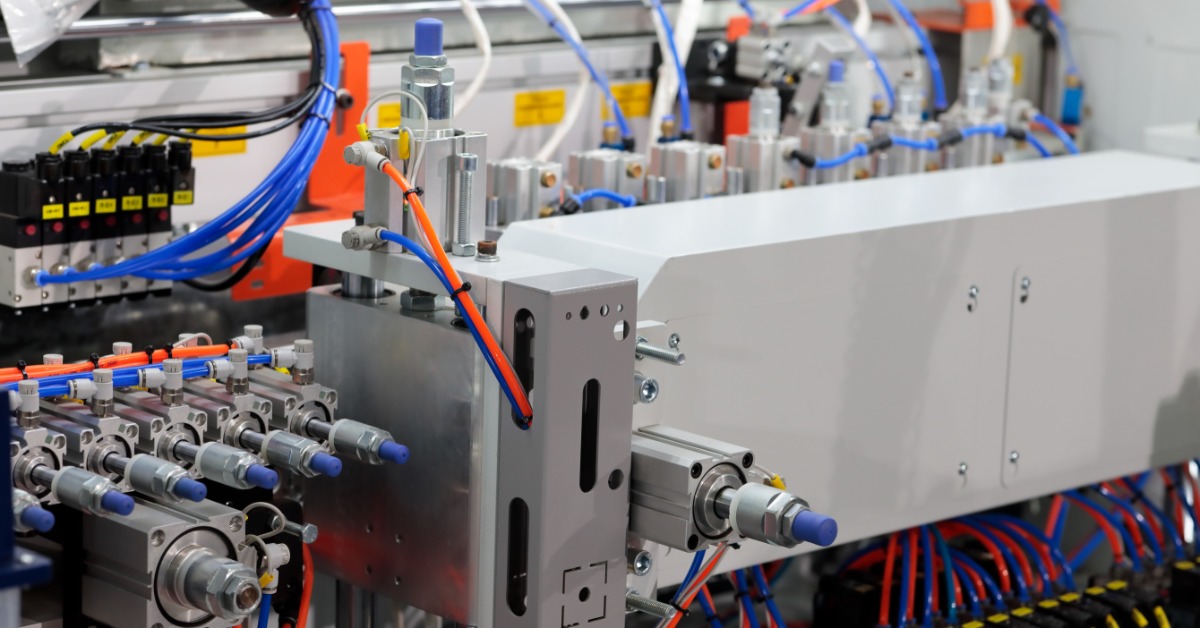 A metal industrial machine with rows of pneumatic cylinders and red and blue tubes connected across its panels.