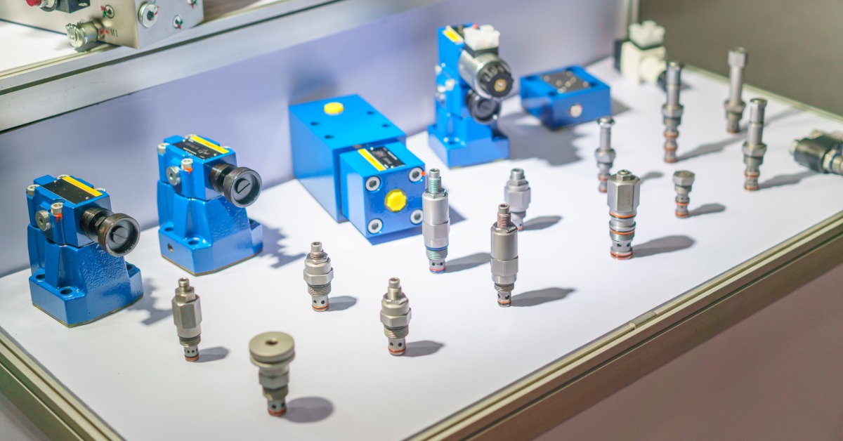 Several blue hydraulic valve components and metal cartridge parts arranged on a white display surface with soft shadows.