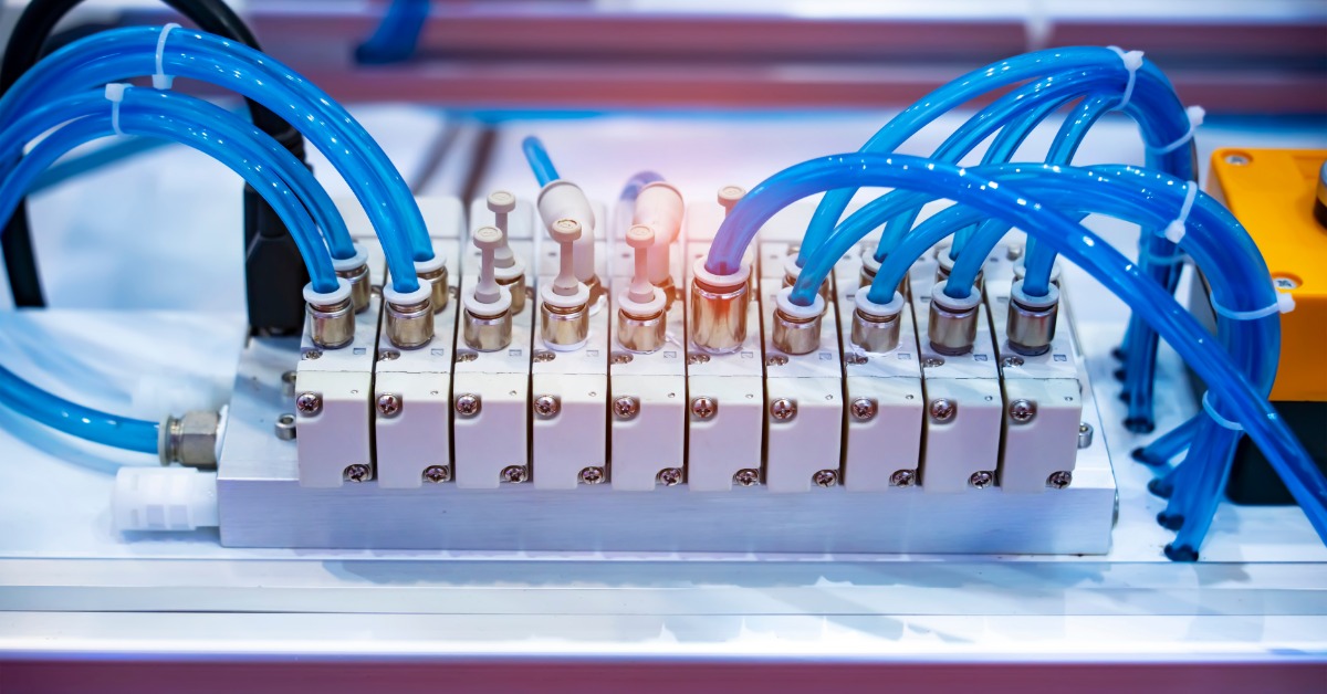 A pneumatic assembly with black hoses, metal valves, gauges, and brass fittings arranged on a white surface.