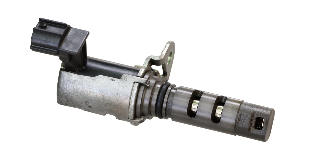 A black-and-silver variable valve timing solenoid resting on a plain white background with its connector visible.
