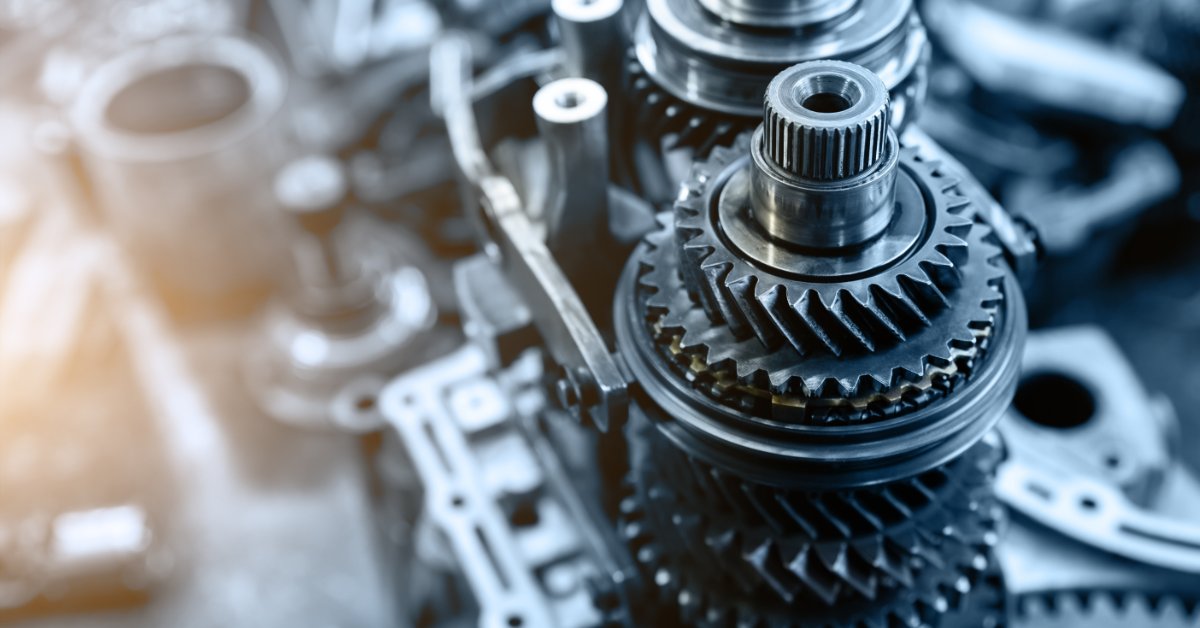 Disassembled automatic transmission gears and metal parts lying on a workbench with bolts and dark tools nearby.